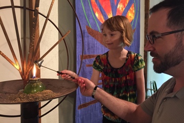 Child and adult lighting chalice during worship service.