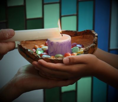 Young and old hands together holding a chalice as the candle in it is being lit. This ritual is part of a UU child's religious education.
